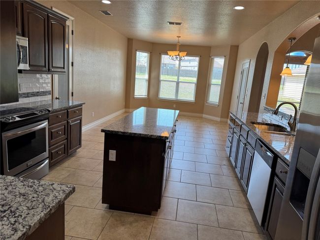Kitchen featuring visible vents, a sink, a center island, stainless steel appliances, and dark stone counters | Image 8