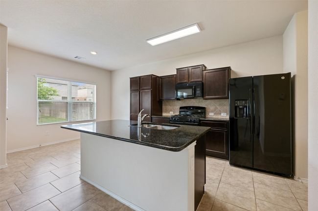 Kitchen with black appliances, a sink, dark brown cabinets, backsplash, and light tile patterned floors | Image 15