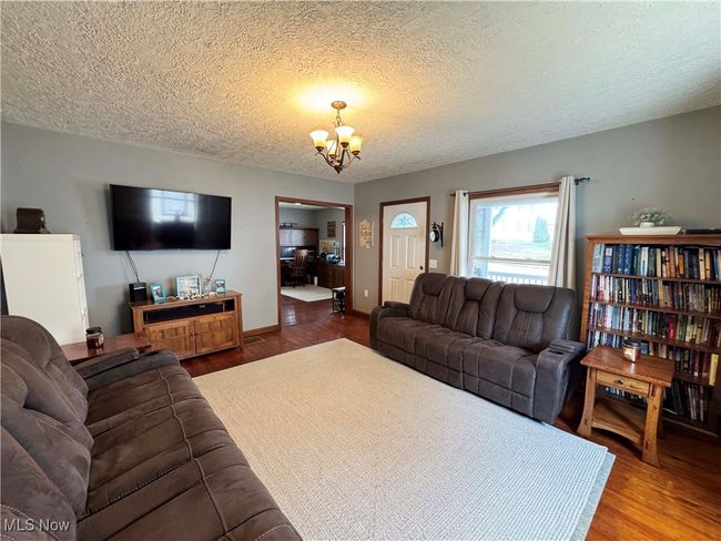 Living area with a textured ceiling, wood finished floors, and a chandelier | Image 10