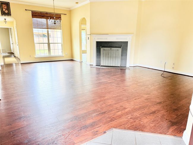 Unfurnished living room with ornamental molding, wood finished floors, arched walkways, baseboards, and a fireplace | Image 6