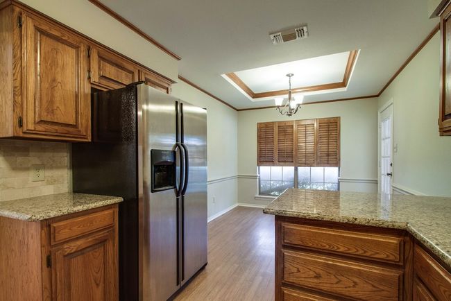 Kitchen featuring stainless steel refrigerator with ice dispenser, a tray ceiling, brown cabinets, a chandelier, and light wood finished floors | Image 13