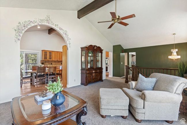 Carpeted living room with arched walkways, ceiling fan, a chandelier, high vaulted ceiling, and beamed ceiling | Image 9