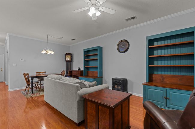 Living area featuring a wood stove, crown molding, ceiling fan, a chandelier, and light wood-type flooring | Image 21