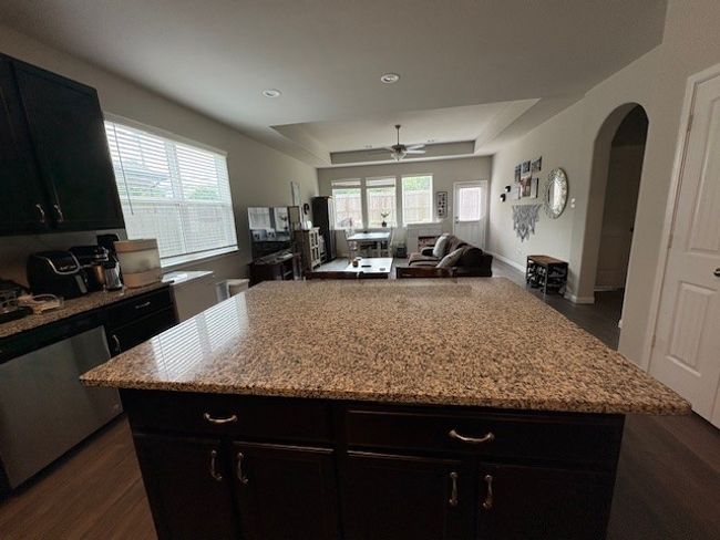 Kitchen featuring a raised ceiling, ceiling fan, arched walkways, dark cabinets, and dark wood-style floors | Image 6