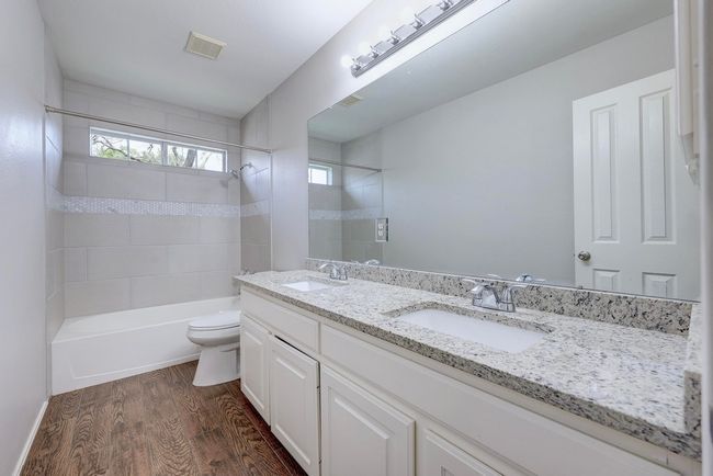Bathroom with toilet, wood finished floors, bathtub / shower combination, and double vanity | Image 29