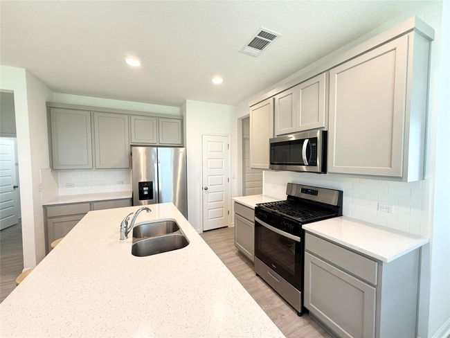 Kitchen with stainless steel appliances, gray cabinetry, a sink, light wood finished floors, and decorative backsplash | Image 14