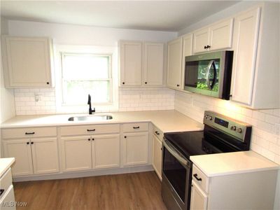 Kitchen featuring light wood-type flooring, tasteful backsplash, stainless steel appliances, and sink | Image 2