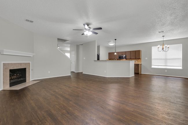 Unfurnished living room with a textured ceiling, a chandelier, a ceiling fan, a tiled fireplace, and dark wood-style floors | Image 8