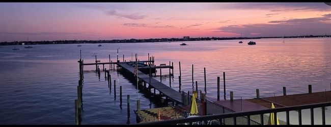 This photo showcases a serene waterfront view at sunset, featuring a dock extending into calm waters with boats moored nearby, under a sky painted in soft hues of pink and purple. Ideal for those seeking a tranquil and picturesque setting. | Image 18