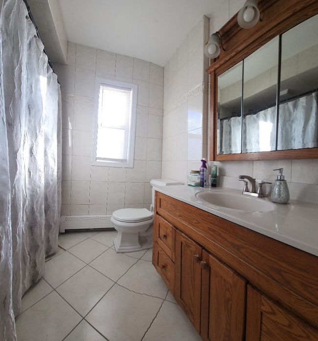Full bathroom featuring tile patterned floors, toilet, vanity, baseboard heating, and tile walls | Image 8