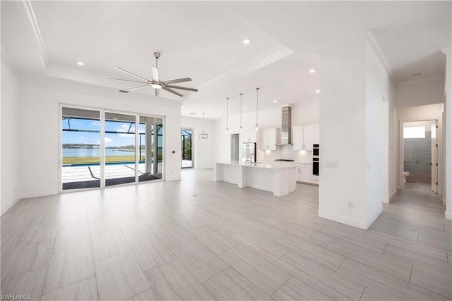 Unfurnished living room featuring a ceiling fan, ornamental molding, a tray ceiling, and recessed lighting | Image 7