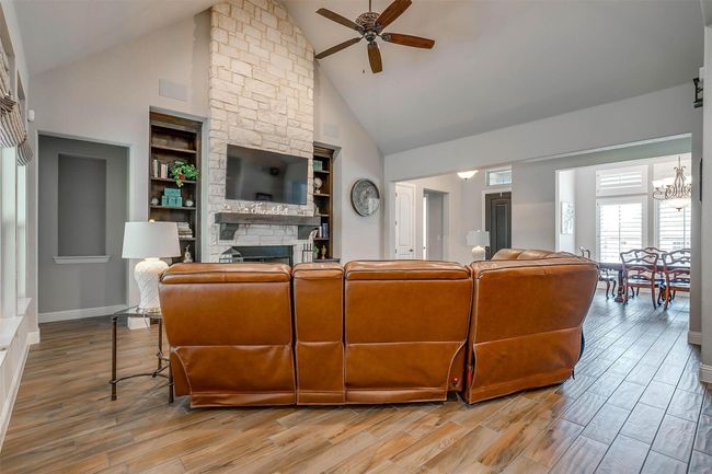 Living area with high vaulted ceiling, a fireplace, ceiling fan, light wood-type flooring, and built in features | Image 6