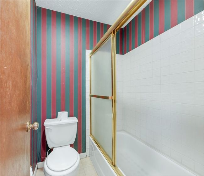Full bath with wallpapered walls, bath / shower combo with glass door, and tile patterned flooring | Image 17