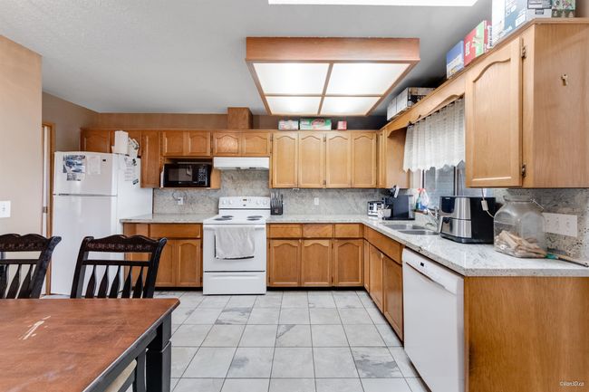 Kitchen featuring white appliances, under cabinet range hood, decorative backsplash, and a sink | Image 7