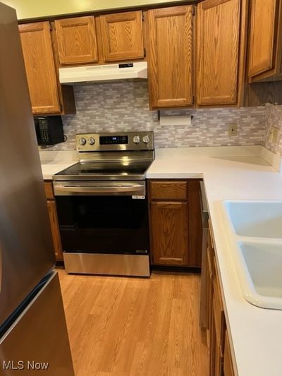 Kitchen featuring light wood-type flooring, sink, appliances with stainless steel finishes, and tasteful backsplash | Image 2