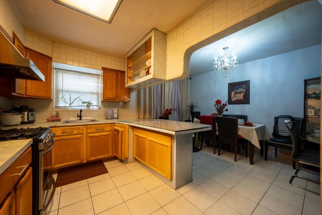 Kitchen with stainless steel range with gas stovetop, a chandelier, a sink, a peninsula, and light tile patterned floors | Image 12