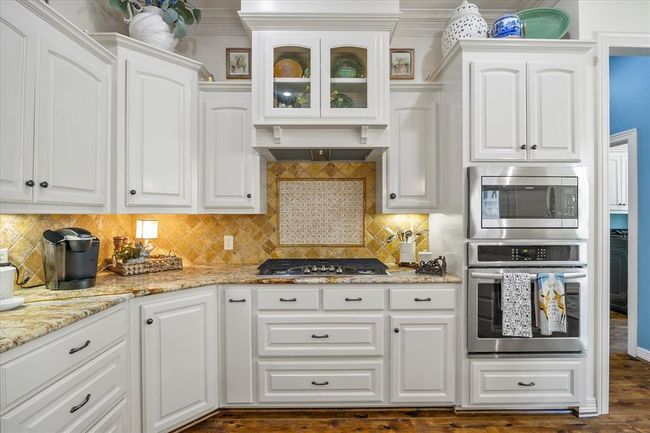 Kitchen featuring backsplash, appliances with stainless steel finishes, dark hardwood / wood-style flooring, and white cabinets | Image 19