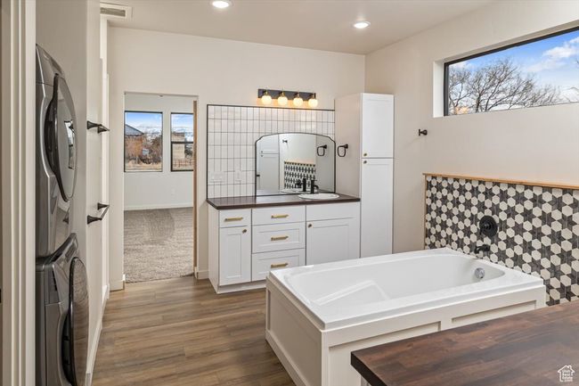 Bathroom with wood-type flooring, vanity, stacked washer and dryer, and a tub to relax in | Image 22