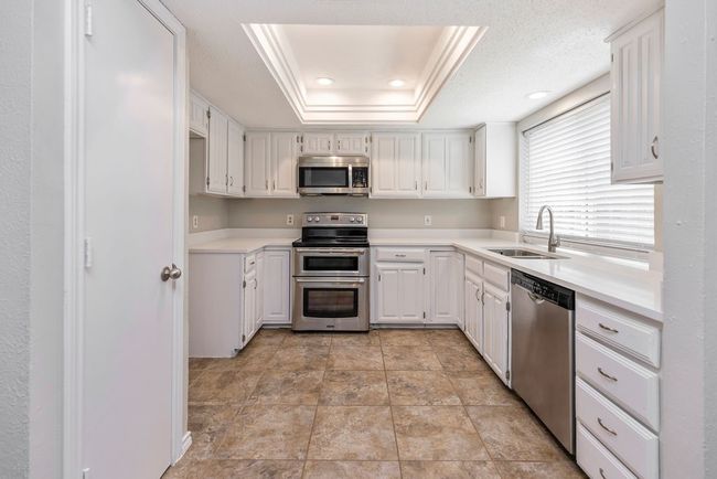 Kitchen with appliances with stainless steel finishes, a sink, white cabinets, light countertops, and recessed lighting | Image 11