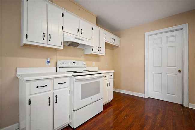 Kitchen with white range with electric stovetop, under cabinet range hood, dark wood finished floors, white cabinetry, and light countertops | Image 9