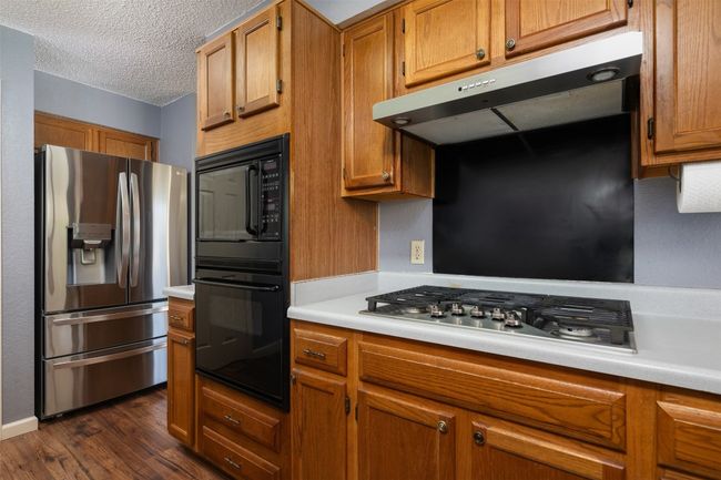 Kitchen featuring exhaust hood, dark wood-type flooring, brown cabinetry, light countertops, and stainless steel appliances | Image 11