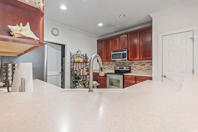 Kitchen with stainless steel appliances, crown molding, reddish brown cabinets, light countertops, and tasteful backsplash | Image 28