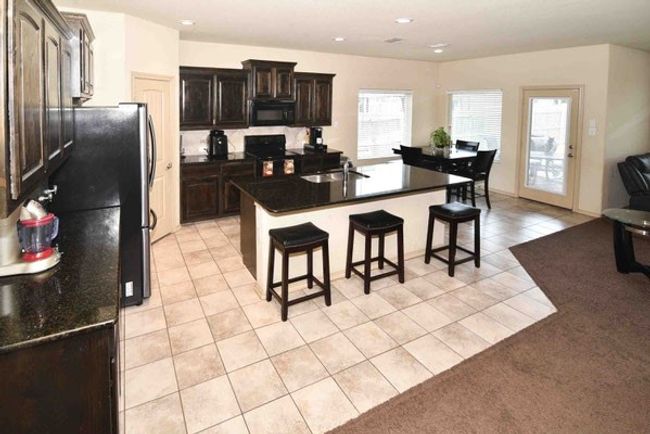 Kitchen featuring black microwave, light tile patterned floors, a kitchen breakfast bar, dark countertops, and recessed lighting | Image 6