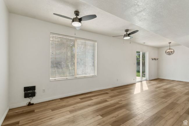 Empty room featuring ceiling fan, light wood-style flooring, a chandelier, a textured ceiling, and baseboards | Image 7