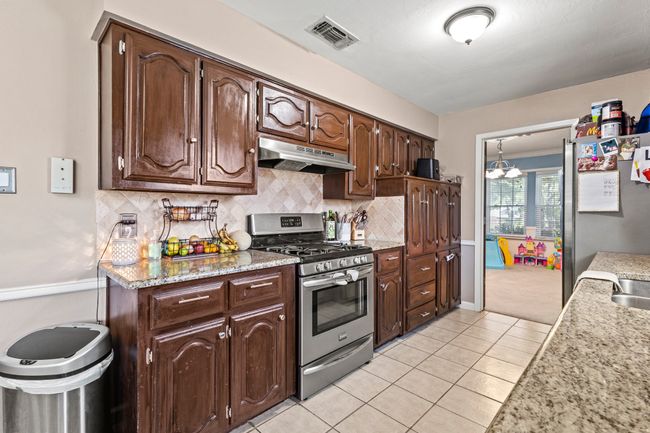 Kitchen with appliances with stainless steel finishes, under cabinet range hood, dark brown cabinets, light tile patterned flooring, and tasteful backsplash | Image 7