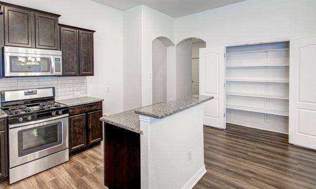 Kitchen featuring stainless steel appliances, dark wood-style flooring, light stone counters, dark brown cabinets, and a kitchen island | Image 22