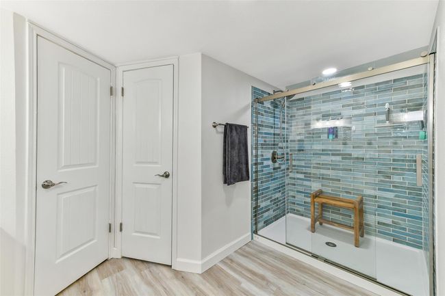 This modern bathroom features a spacious glass-enclosed shower with stylish blue tile & dual shower heads offering a fresh and contemporary feel. | Image 17