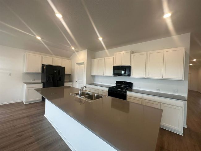 Kitchen with black appliances, a sink, white cabinetry, a large island, and dark wood-style floors | Image 13