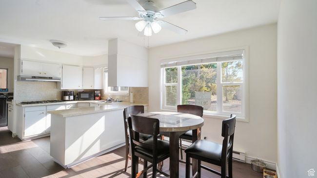 Kitchen with under cabinet range hood, black microwave, a peninsula, and tasteful backsplash | Image 7