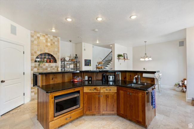 Kitchen with stainless steel microwave, a large island with sink, a chandelier, dark stone counters, and a textured ceiling | Image 7