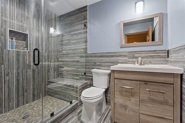 Full bath featuring a wainscoted wall, tile walls, toilet, a stall shower, and vanity | Image 69