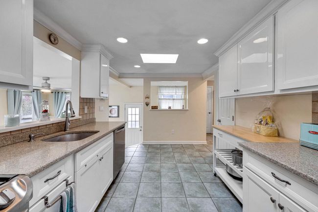 Kitchen with stainless steel dishwasher, a sink, tasteful backsplash, baseboards, and white cabinetry | Image 22