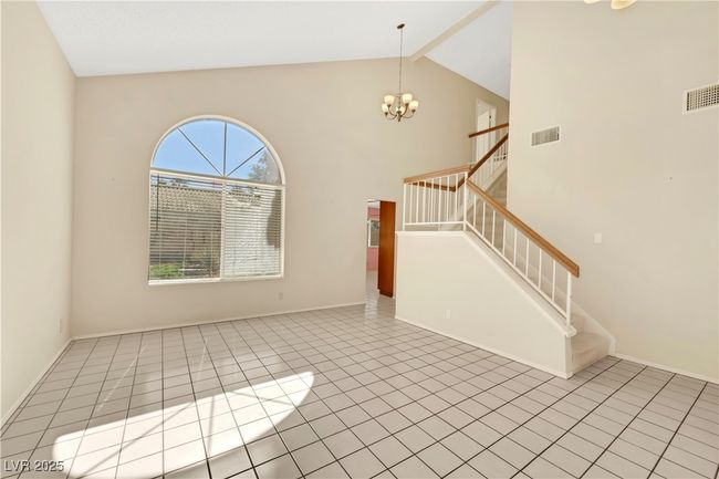 Unfurnished living room featuring an inviting chandelier, stairway, visible vents, and beamed ceiling | Image 6