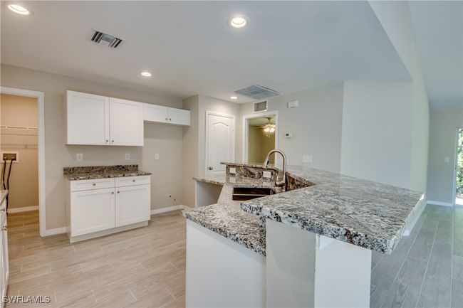 Kitchen with wood finish floors, recessed lighting, visible vents, white cabinetry, and a sink | Image 24