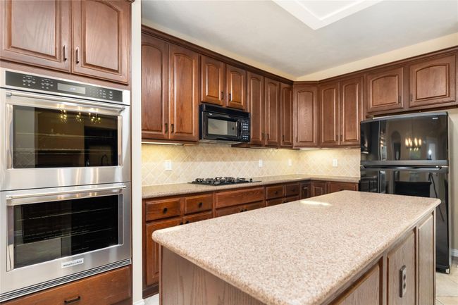 Tall ceilings and rich wood cabinetry bring warmth and sophistication to the kitchen, complete with a central island and sleek stainless steel double ovens. | Image 16