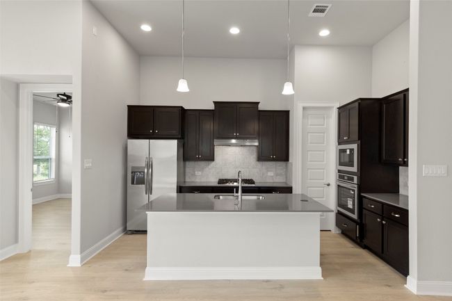 Kitchen with stainless steel appliances, backsplash, a center island with sink, a ceiling fan, and light wood-type flooring | Image 18
