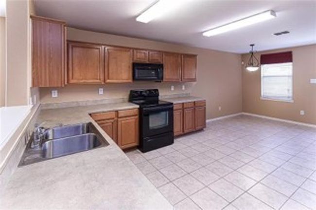 Kitchen featuring black appliances, light countertops, brown cabinetry, pendant lighting, and light tile patterned flooring | Image 5