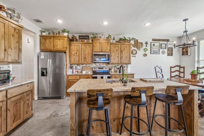 Kitchen with appliances with stainless steel finishes, a sink, light stone countertops, a kitchen breakfast bar, and recessed lighting | Image 7