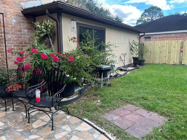 This photo showcases a cozy backyard with a small patio area featuring metal chairs and lush greenery, including vibrant flowers. The space is enclosed by a wooden fence and a brick wall, offering a private and inviting atmosphere for outdoor relaxation. | Image 6