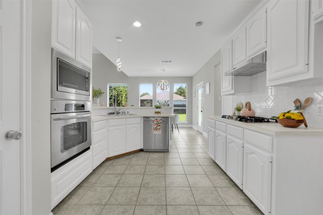 Kitchen with appliances with stainless steel finishes, under cabinet range hood, a peninsula, tasteful backsplash, and white cabinets | Image 9