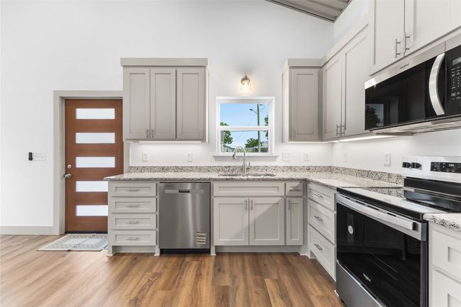 Kitchen with stainless steel appliances, a sink, wood finished floors, and light stone countertops | Image 13