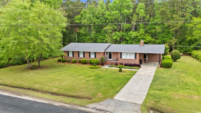 Ranch-style house featuring an attached carport, a wooded view, a chimney, concrete driveway, and brick siding | Image 23