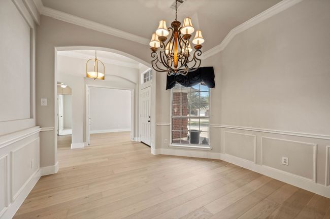 Unfurnished dining area with a notable chandelier, crown molding, light wood-style flooring, a decorative wall, and arched walkways | Image 8