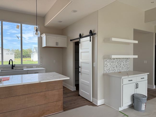 Kitchen with open shelves, a barn door, white cabinetry, light stone counters, and decorative light fixtures | Image 8