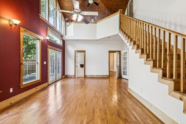 Unfurnished living room featuring french doors, high vaulted ceiling, wood finished floors, a ceiling fan, and stairway | Image 17