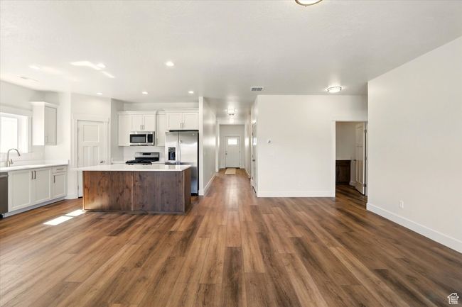 Kitchen with stainless steel appliances, a center island, white cabinetry, a sink, and dark wood-style floors | Image 8